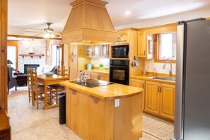 A kitchen with wooden cabinets, a central island, a microwave, and a refrigerator. - Get-A-Way Beach Chalet (Grande-Digue)