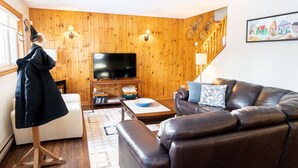 A cozy living room with a leather sofa, a flat-screen TV, wooden walls, and a staircase.