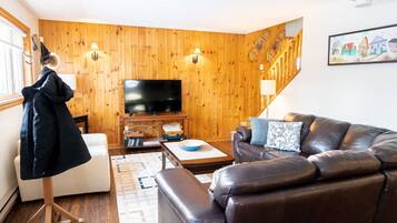 A cozy living room with a leather sofa, a flat-screen TV, wooden walls, and a staircase.