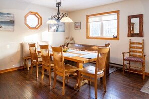 A dining area with a wooden table and chairs, a hexagonal window, and a large mirror on the wall. - Get-A-Way Beach Chalet (Grande-Digue)