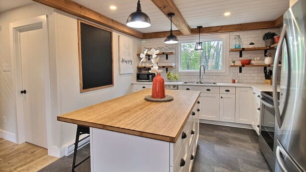 Una cocina con armarios blancos, una isla de madera, iluminación colgante y un refrigerador de acero inoxidable.