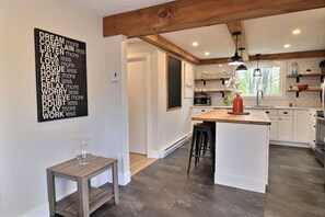 Una cocina moderna con armarios blancos, una isla de madera y una lámpara colgante negra.