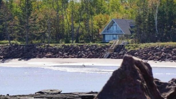 A house with a dock extending into a body of water, surrounded by trees and a rocky shoreline. - East Coastal- Waterfront Cottage (Beaubassin-est)