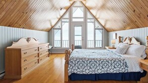 A bedroom with a sloped ceiling, a bed with a patterned bedspread, a dresser, and a nightstand with a lamp. - East Coastal- Waterfront Cottage (Beaubassin-est)