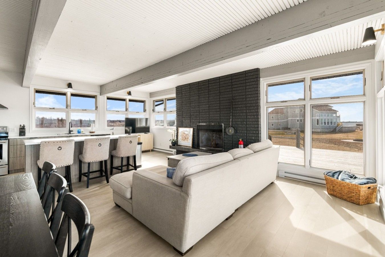 A modern kitchen with a large island, a dining area with a black table, and a living room with a sofa and a fireplace.