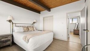 Une chambre avec un grand lit, un plancher en bois et un plafond avec des poutres apparentes.