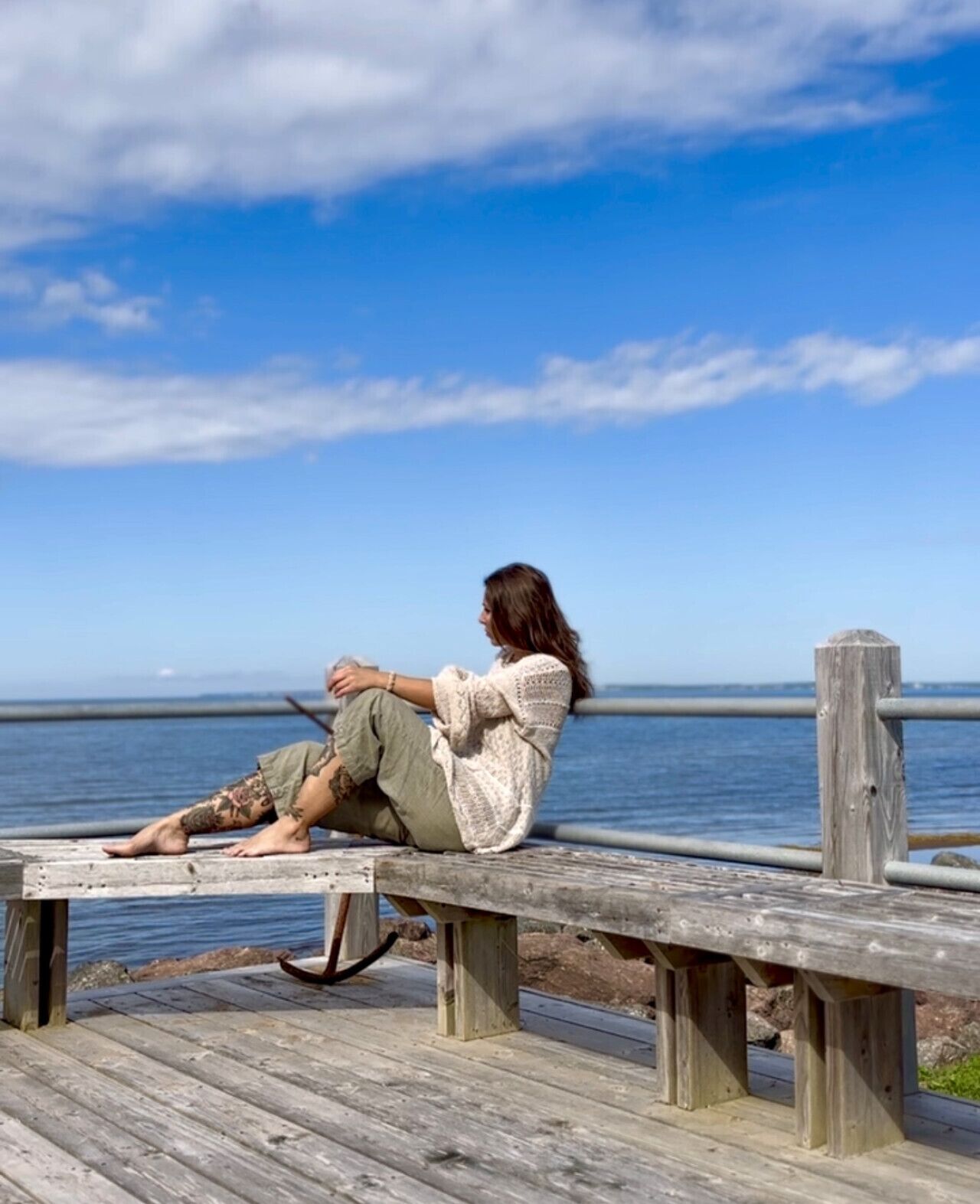 Eine Person sitzt auf einer Holzbank am Wasser und blickt aufs Meer.