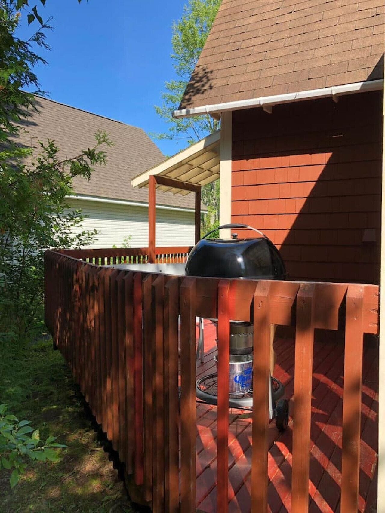 Eine Holzterrasse mit Grill, einer überdachten Veranda und einem Haus im Hintergrund.
