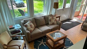 Una sala de estar con un sofá, un sillón, una mesa de centro y vistas al exterior a través de amplios ventanales.
