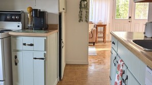 Una cocina con suelo de madera, armarios blancos y una cafetera.