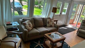 A living room with a sofa, armchairs, a coffee table, and a window with a view of the outdoors. - Rustic Retreat- Bois Joli Beach (Beaubassin-est)