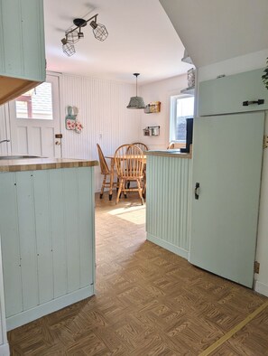 Une cuisine avec des meubles de rangement en bois, une table à manger avec des chaises et une fenêtre.