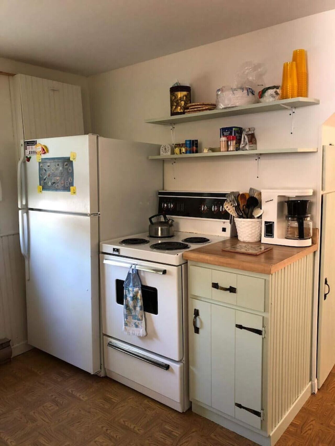Eine kleine Küche mit Kühlschrank, Herd, Mikrowelle und einer Holzarbeitsplatte.