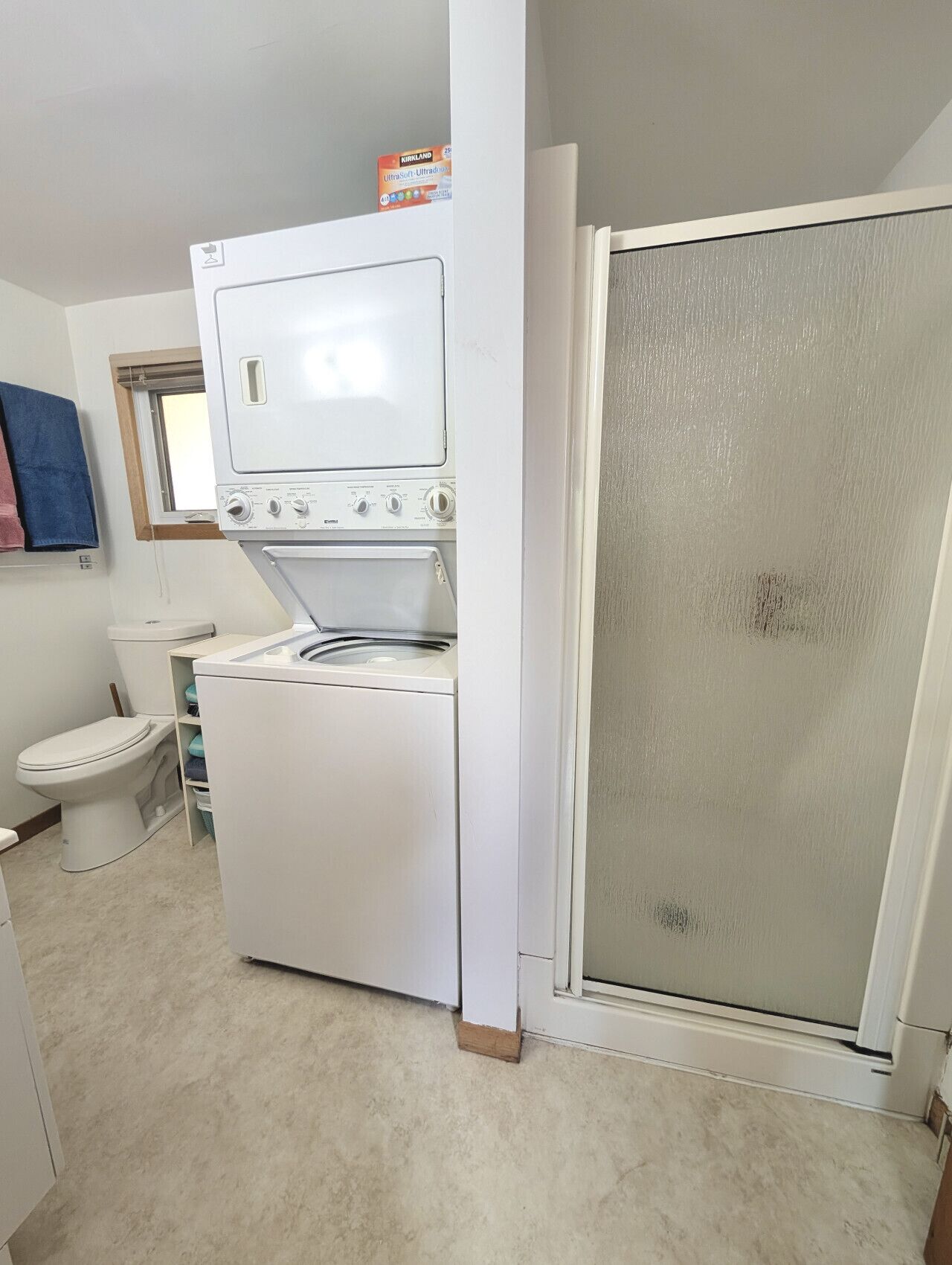 A compact laundry room with a washer and dryer, a toilet, and a shower enclosure.