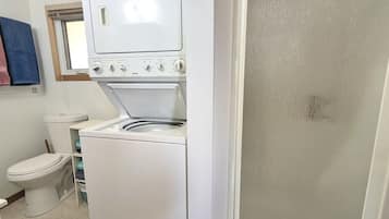 A compact laundry room with a washer and dryer, a toilet, and a shower enclosure.