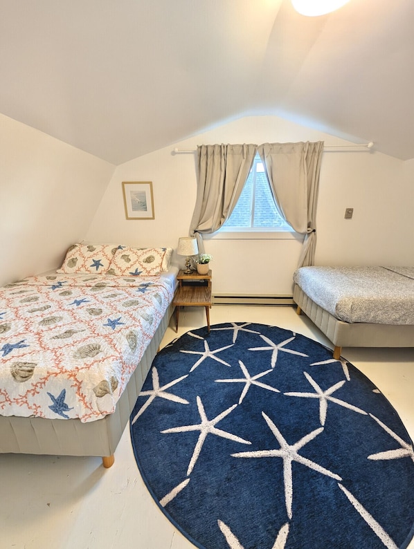Une chambre avec deux lits, une fenêtre avec des rideaux, une table de chevet avec une lampe et un tapis orné de motifs en forme d’étoiles.