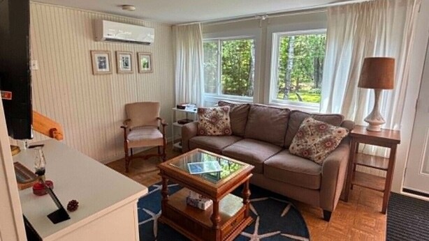 A living room with a sofa, armchair, coffee table, and a lamp. - Rustic Retreat- Bois Joli Beach (Beaubassin-est)