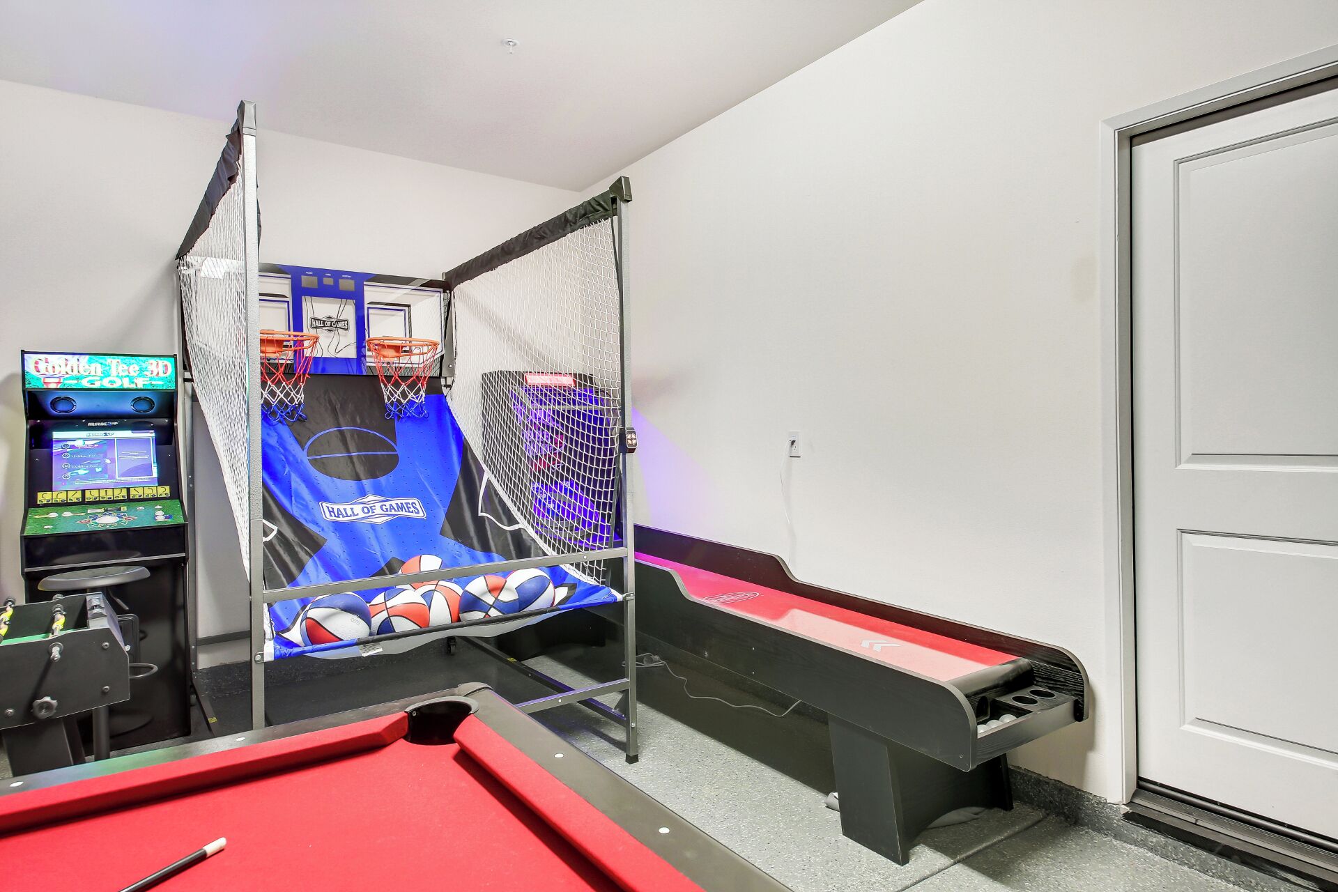 A pool table with a red felt surface, a pool cue, and a blue and black arcade game titled "Hall of Games" with a basketball hoop.