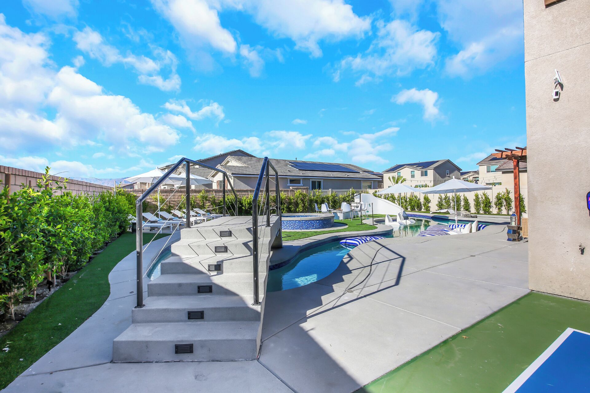 A residential area with a swimming pool, a staircase leading to a deck, and houses in the background.
