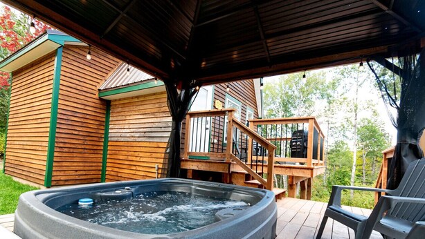 A hot tub on a wooden deck with a covered area and a wooden deck chair.