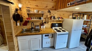 A compact kitchen with wooden walls, a stove, a sink, and a refrigerator.