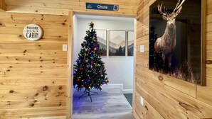 A cabin interior with a Christmas tree, a deer taxidermy, and a sign reading "Welcome to the Cabin."