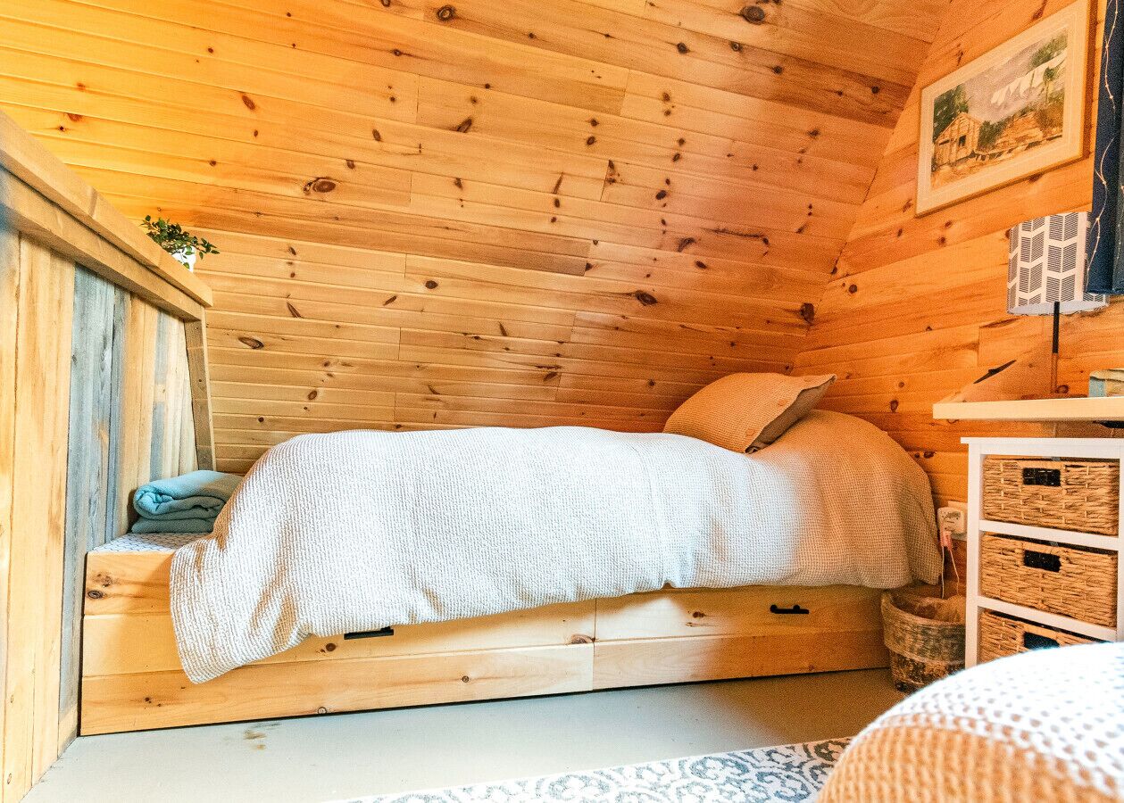 A cozy wooden cabin bedroom with a bed, a small bedside table, and a wall-mounted picture.