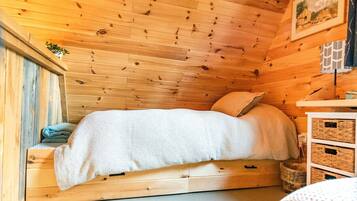 A cozy wooden cabin bedroom with a bed, a small bedside table, and a wall-mounted picture.