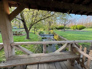 Ett trädäck med utsikt över en trädgård med ett litet vattenfall, picknickbord och en gräsyta.