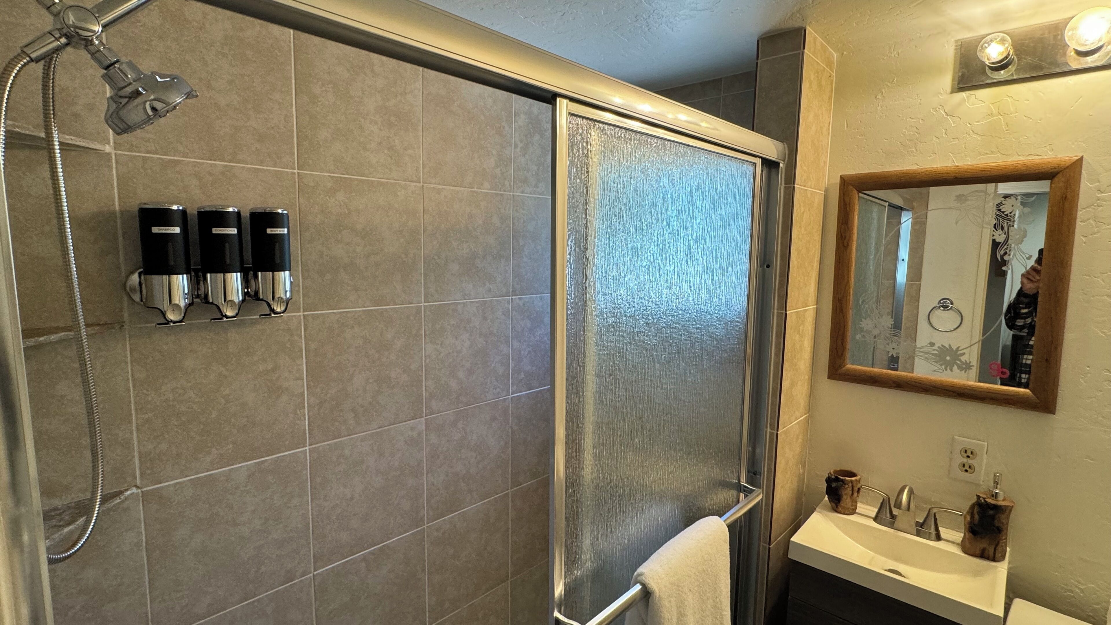 Een douche met een glazen deur, een handdoekrek en twee shampoos Dispensers.
