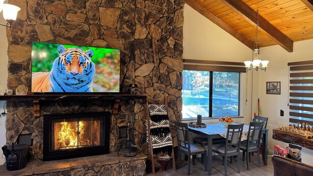 Ein Kamin aus Stein mit Fernseher, der eine Tiger zeigt, ein Essbereich mit Stühlen und Blick ins Freie.