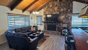 Ein gemütliches Wohnzimmer mit Kamin aus Stein, einer Ledersofa und einem flachbildfernseher, der darüber angebracht ist.