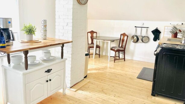 A kitchen with a white brick wall, wooden floor, a coffee machine, a plant, and a stove. - Finn's Studio Suite Apartment, Alma, Fundy Park (Alma)