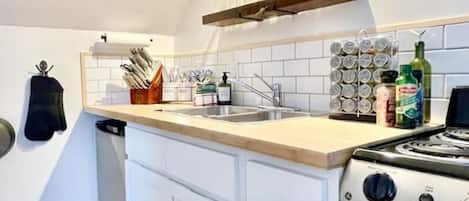 A compact kitchen with white cabinets, a wooden countertop, a built-in oven, and a hanging light fixture.