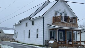 A white two-story house with a wooden balcony and a covered porch. - Finn's Studio Suite Apartment, Alma, Fundy Park (Alma)