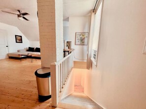 A staircase leading to a second floor with a white railing, a trash can, a ceiling fan, and a framed artwork on the wall. - Finn's Studio Suite Apartment, Alma, Fundy Park (Alma)