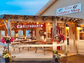 Una estructura de madera con un letrero que dice "Alma Lobster Shop" y un letrero de "RESTAURANT" sobre un área de asientos al aire libre techada.