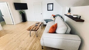 A modern living room with a grey sofa, a wooden coffee table, and a flat-screen TV mounted on the wall. - Finn's Studio Suite Apartment, Alma, Fundy Park (Alma)
