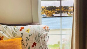 A bed with floral bedding and a view of a lake and buildings through a window. - Finn's Studio Suite Apartment, Alma, Fundy Park (Alma)