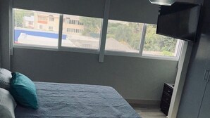Un dormitorio con una cama, ventana, televisor y escritorio.
