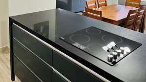 Una cocina moderna con encimera negra y estufa integrada, comedor con sillas de madera y una mesa, y un ventanal con vistas a la ciudad.