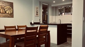 Una cocina moderna con una isla central, mesa de comedor de madera con sillas y una lámpara colgante.