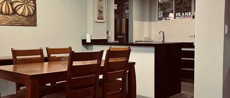 A modern kitchen with a central island, wooden dining table with chairs, and a ceiling light fixture.
