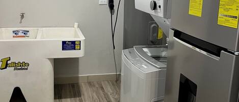 A compact kitchen with a Whirlpool refrigerator, a built-in washer, and a sink with a white countertop.
