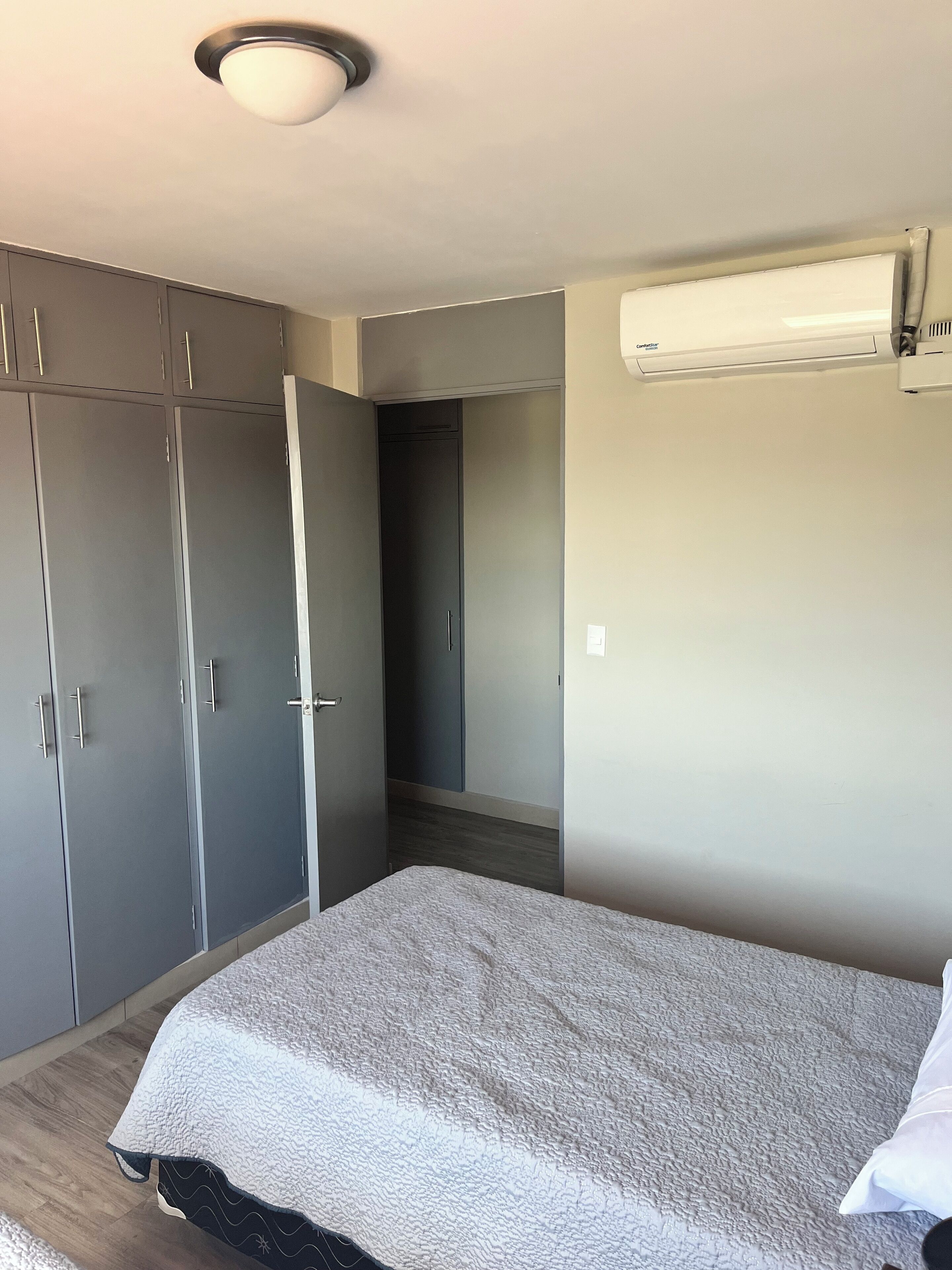 A bedroom with a bed, grey wardrobe, and an air conditioning unit.