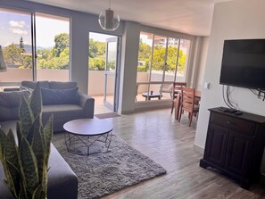 Een moderne woonkamer met een bank, een ronde salontafel, een televisie en een balkon met tuinmeubilair.