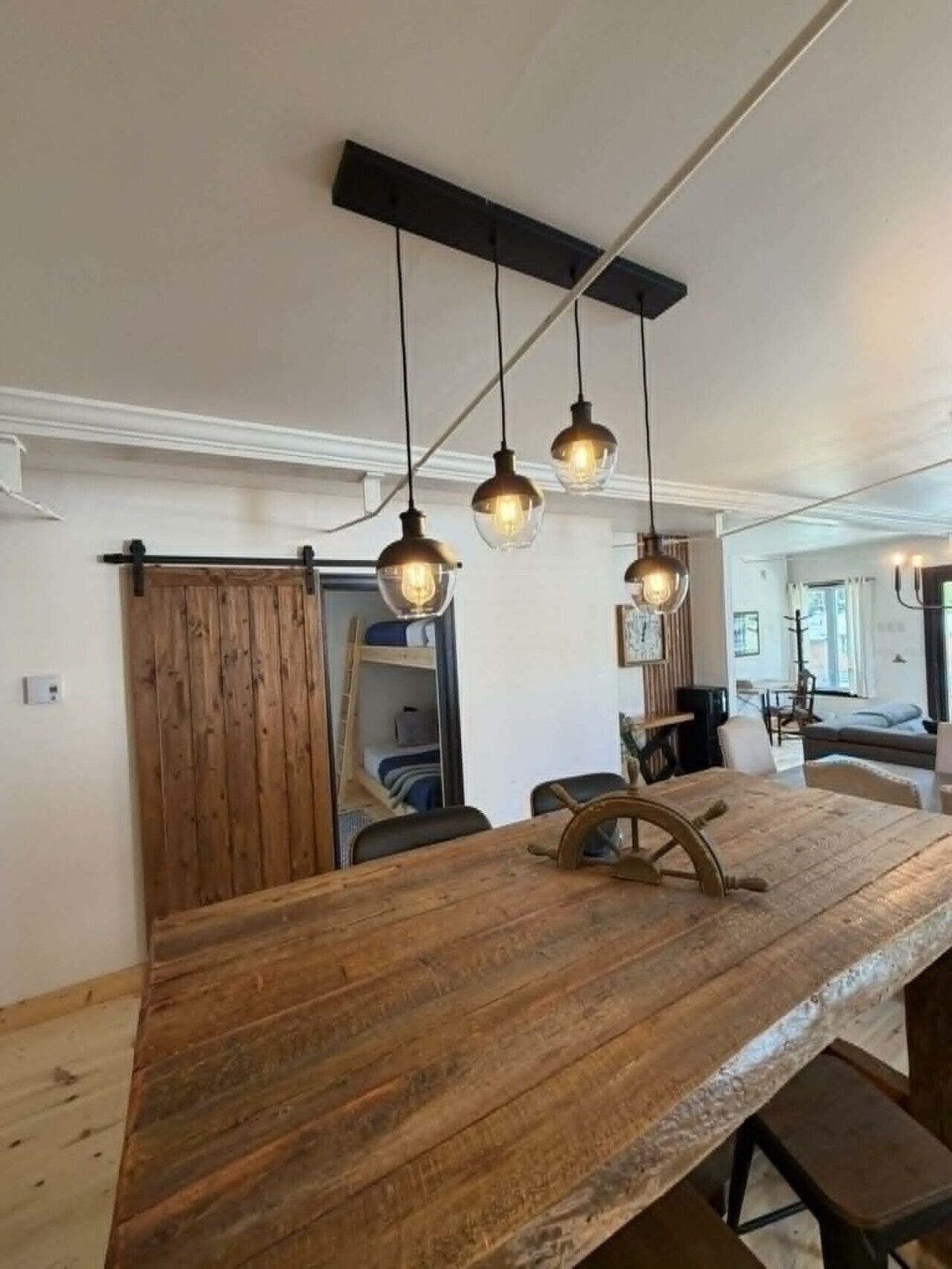 A rustic wooden table with a ship's wheel centerpiece, hanging pendant lights, and a wooden barn door.