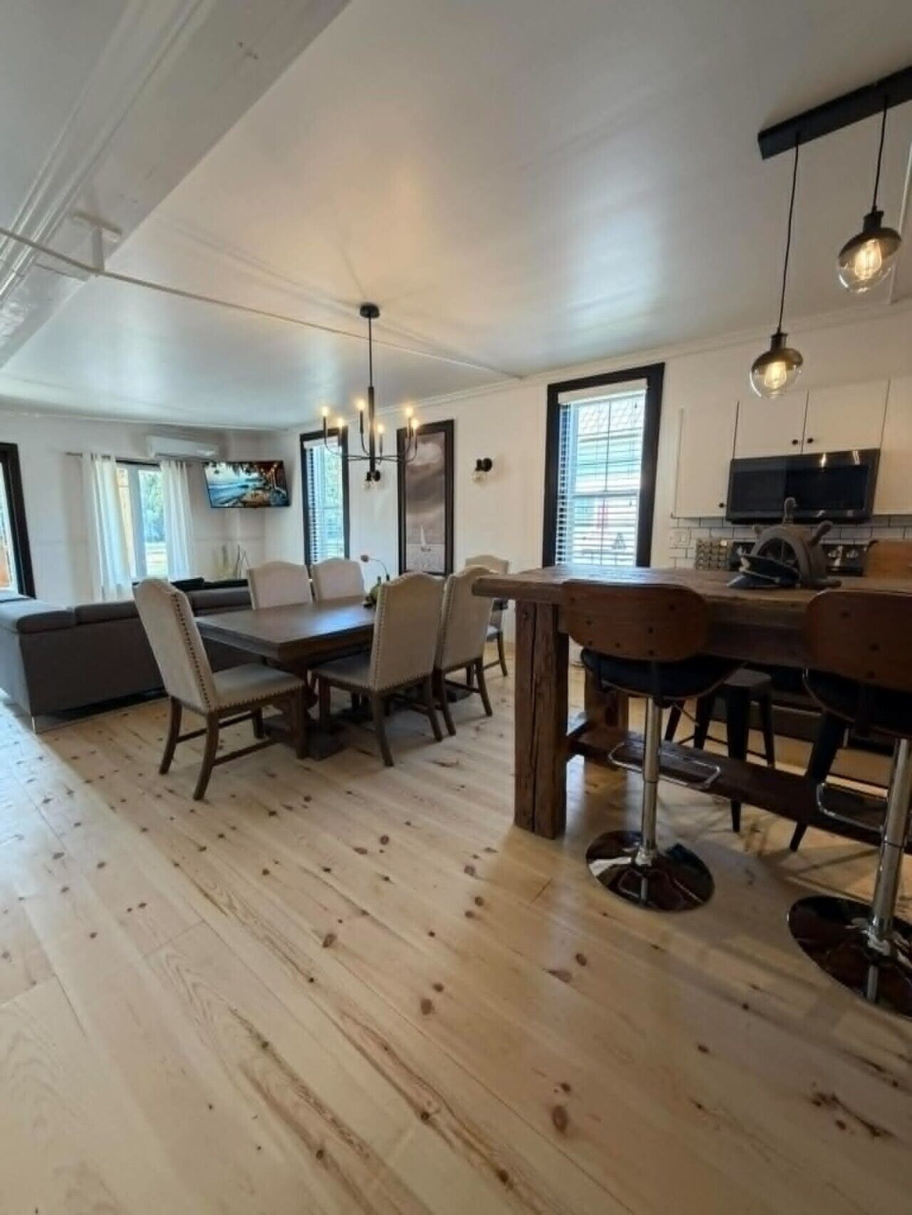 A spacious dining area with a wooden table and chairs, a kitchen area with a microwave and stove, and a television mounted on the wall.