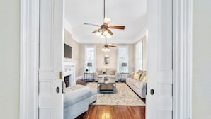 A spacious living room with a ceiling fan, a fireplace, and a large window. - Victorian Manor: Downtown Apt, near Silver Springs & Fort King Historic Park (Ocala)