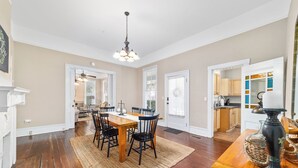 A spacious dining area with a wooden table and chairs, a chandelier, and a kitchen visible through an open door. - Victorian Manor: Downtown Apt, near Silver Springs & Fort King Historic Park (Ocala)